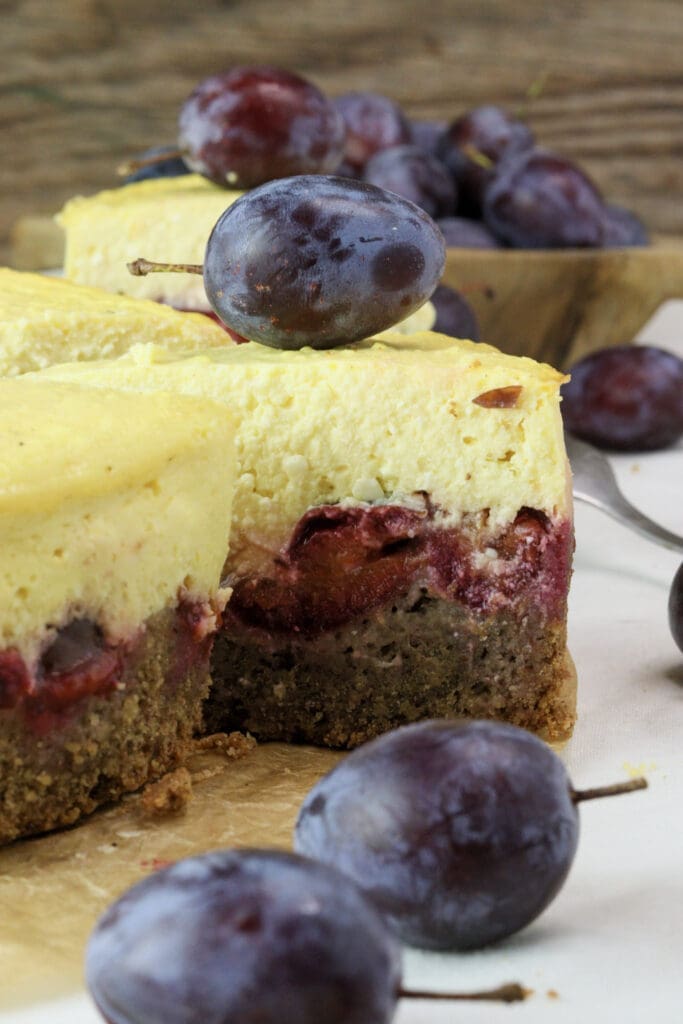 Sliced plum cheesecake with plums in the background.